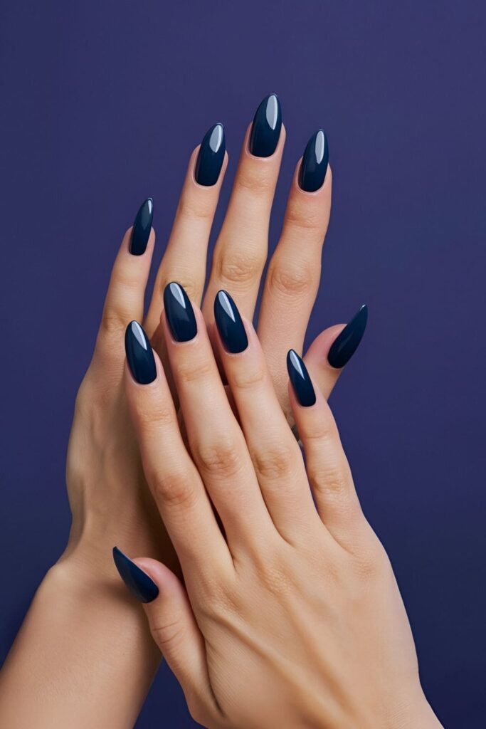 A hand displaying deep ink blue acrylic nails, bold and sophisticated, with a possible watercolor effect or ink design for added elegance