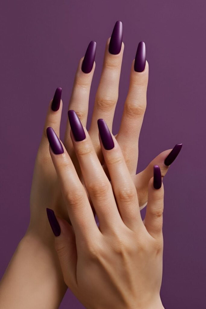 A hand displaying deep plum purple acrylic nails with a matte finish, sophisticated and dramatic, with optional glitter for a luxurious look