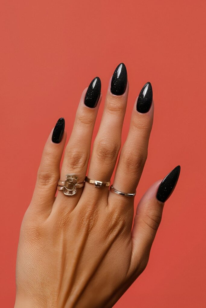 A hand with jet black acrylic nails adorned with glitter, combining classic elegance and glamour, perfect for parties