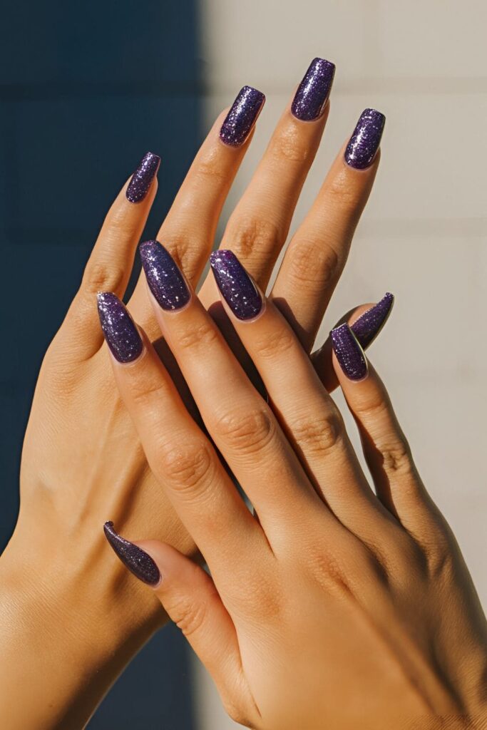 Acrylic nails covered in purple glitter, with some nails fully glittered and others with glitter tips, sparkling in the sunlight