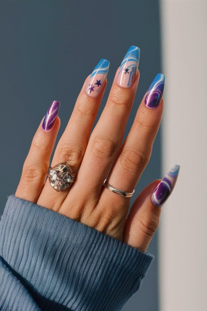 Acrylic nails with a cosmic effect, featuring blue, purple, and white swirls with glitter stars