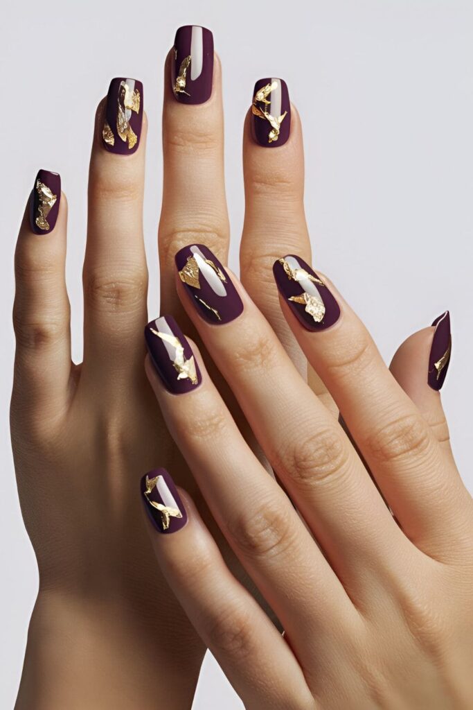 Acrylic nails with a dark purple base, accented with pieces of gold leaf for a luxurious and glamorous look