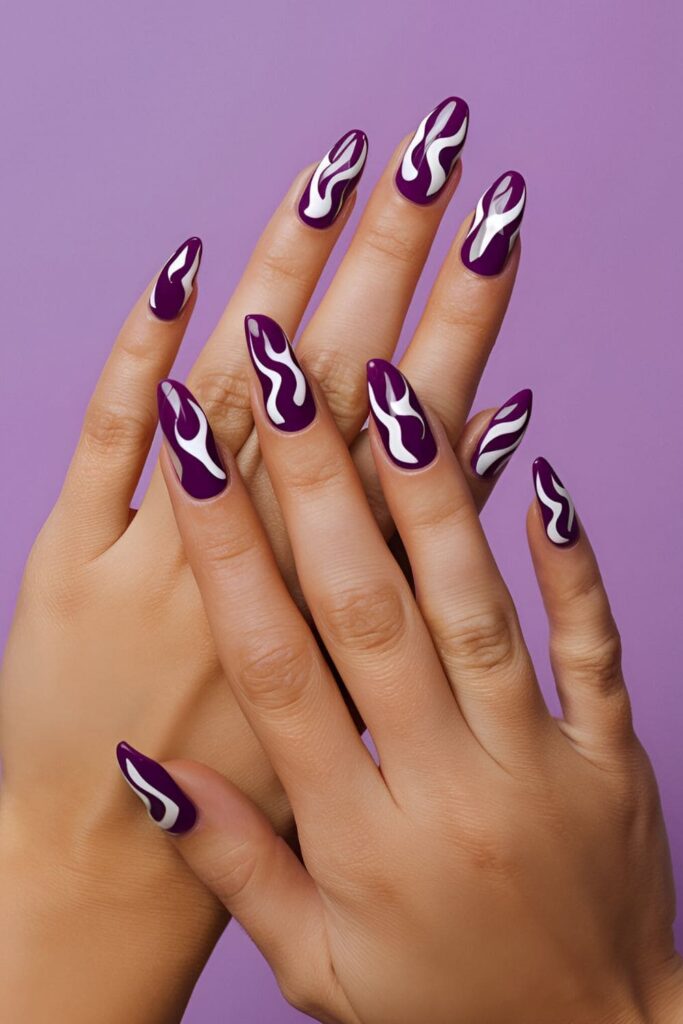 Acrylic nails with a purple base, featuring bold flame designs in white or black, creating a fiery and edgy look