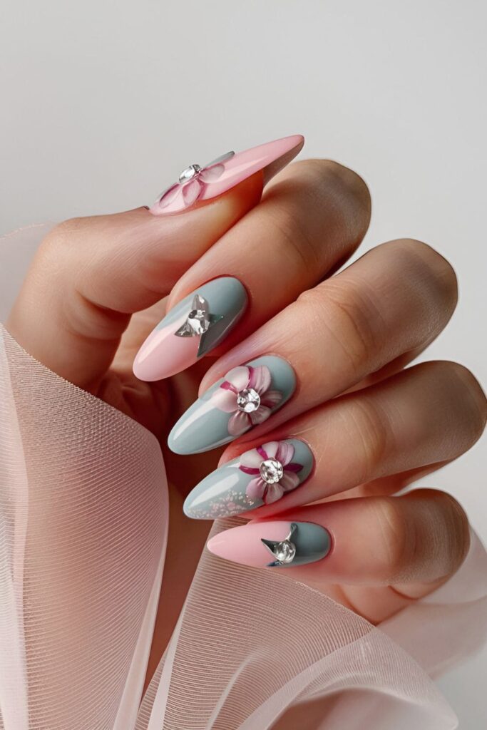 Acrylic nails with soft base colors, painted floral designs, and rhinestones at the center of each flower