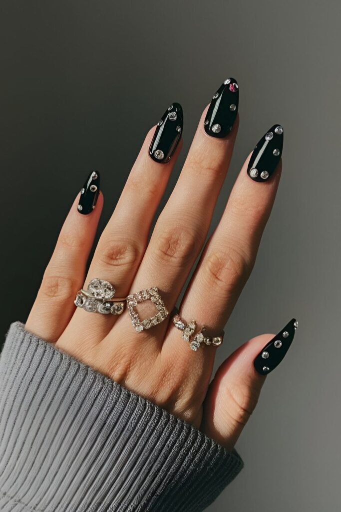 Black acrylic nails decorated with tiny and large jewel accents, creating a luxurious and glamorous style