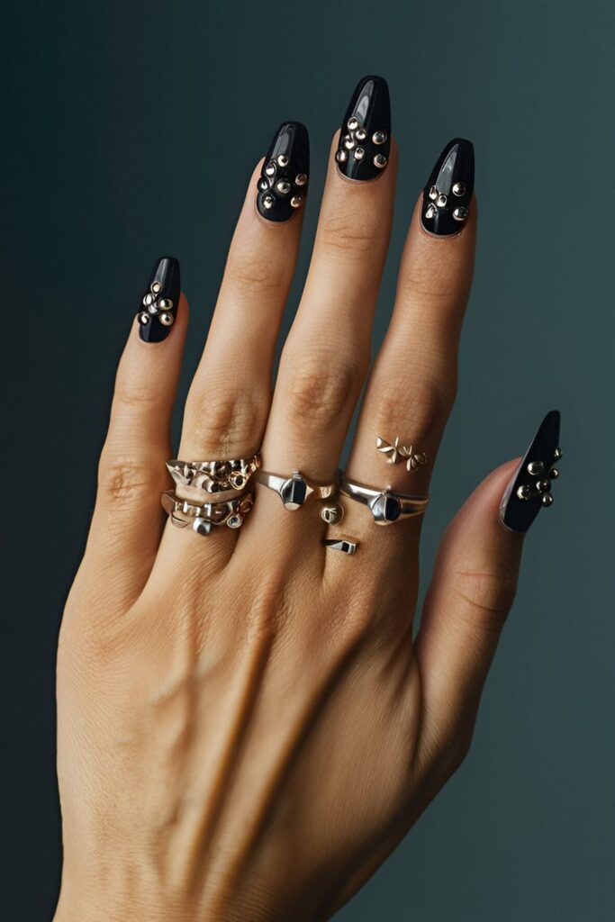 Black acrylic nails featuring silver studs in various sizes, perfect for an edgy, rocker-chic look