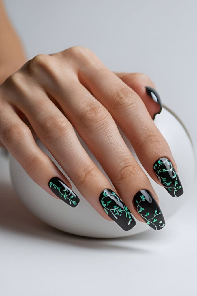 Black acrylic nails with delicate vine patterns in green and white, adding elegance and nature-inspired beauty