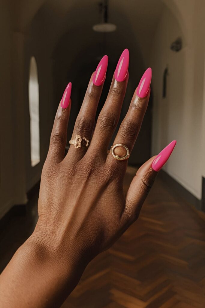 Bold pink stiletto-shaped acrylic nails, designed to make a dramatic statement on dark skin tones