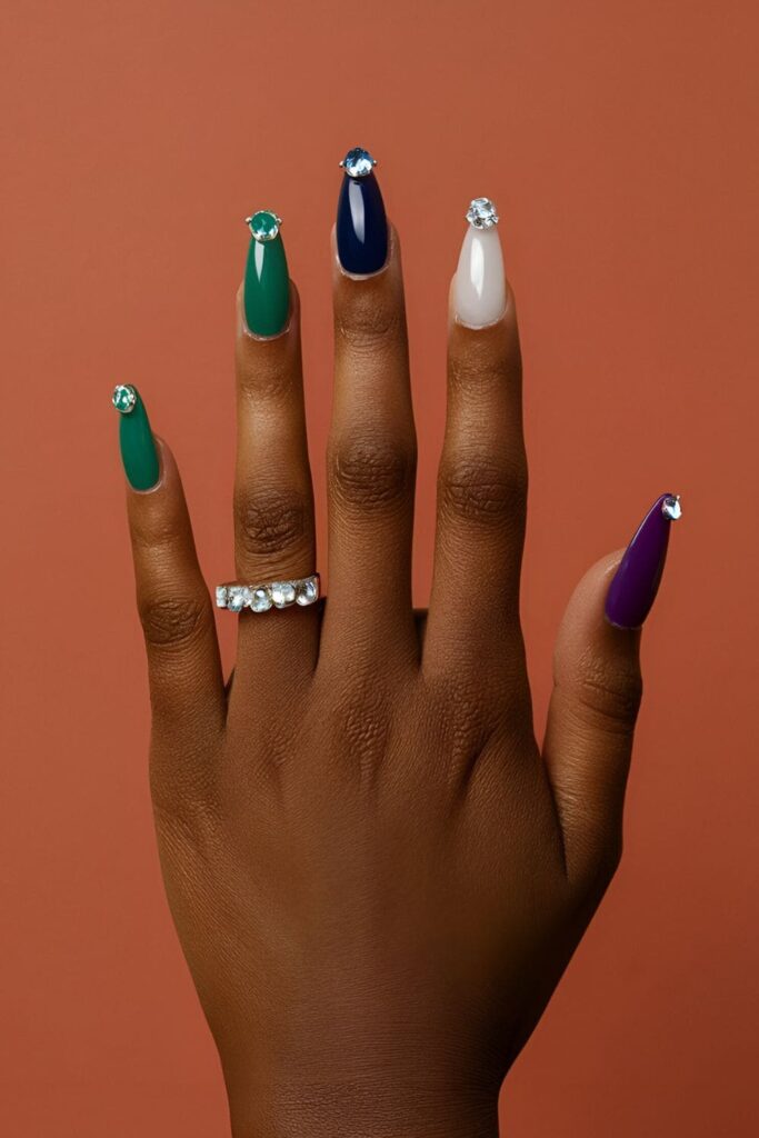 Dark-skinned hands with emerald, sapphire, and amethyst acrylic nails, combined with rhinestones