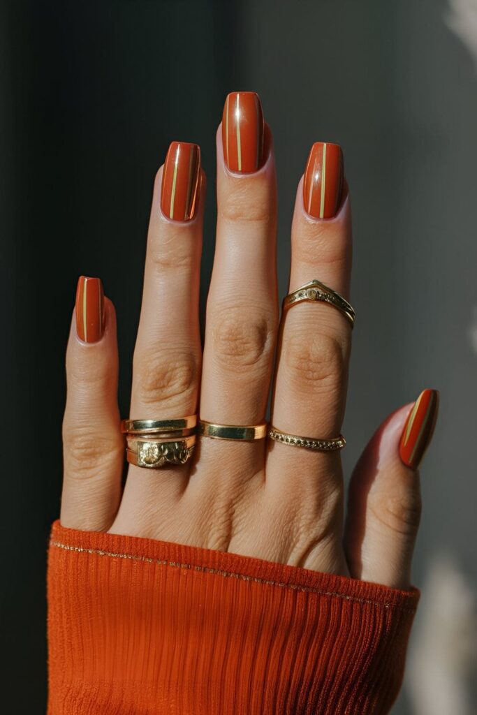 Chic gold striped acrylic nails on an orange base, sophisticated and stylish nail art