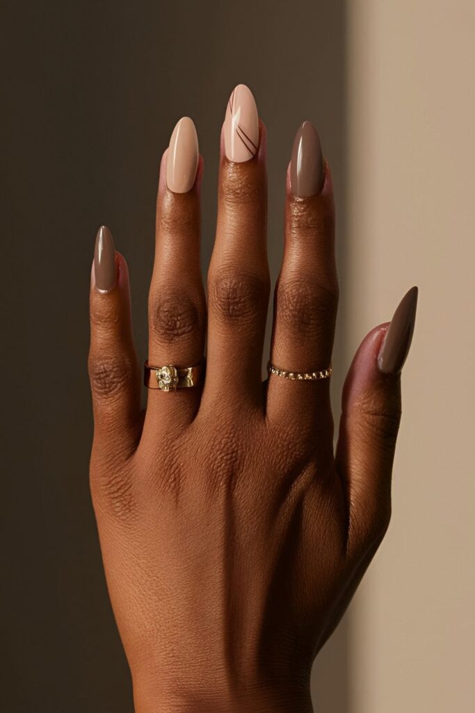 Dark-skinned hands with warm beige and cool taupe acrylic nails, adorned with subtle line designs