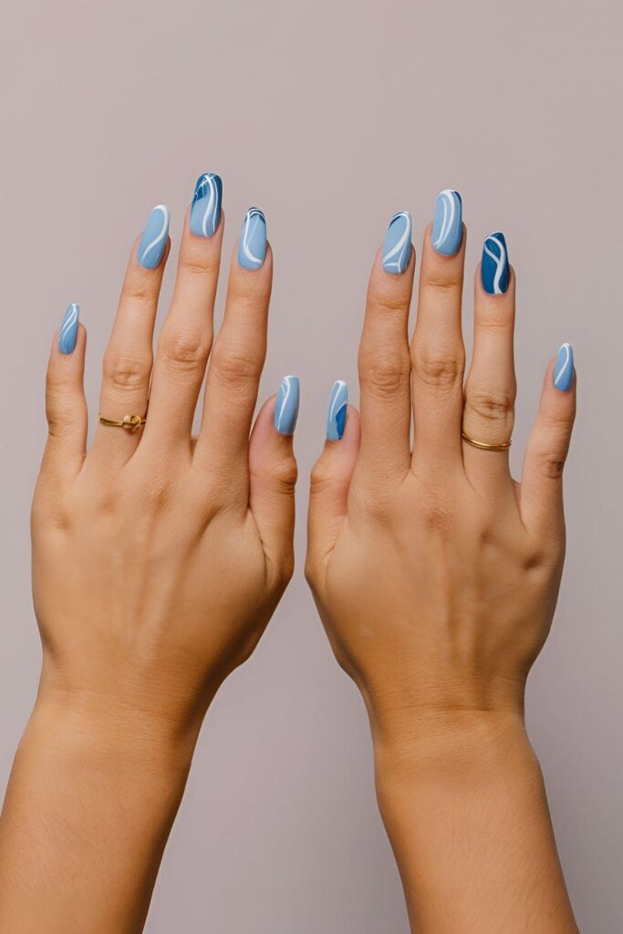 Close-up of blue marble acrylic nails, combining light and dark blue with white swirls