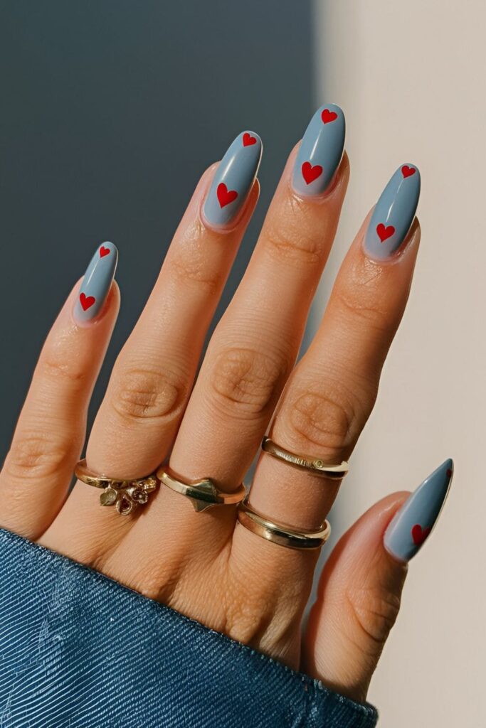 Denim blue acrylic nails with small red or pink hearts painted on each nail for a whimsical touch