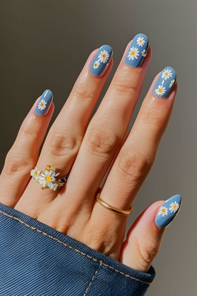 Denim blue acrylic nails with tiny white and yellow daisies painted on each nail for a cute spring look