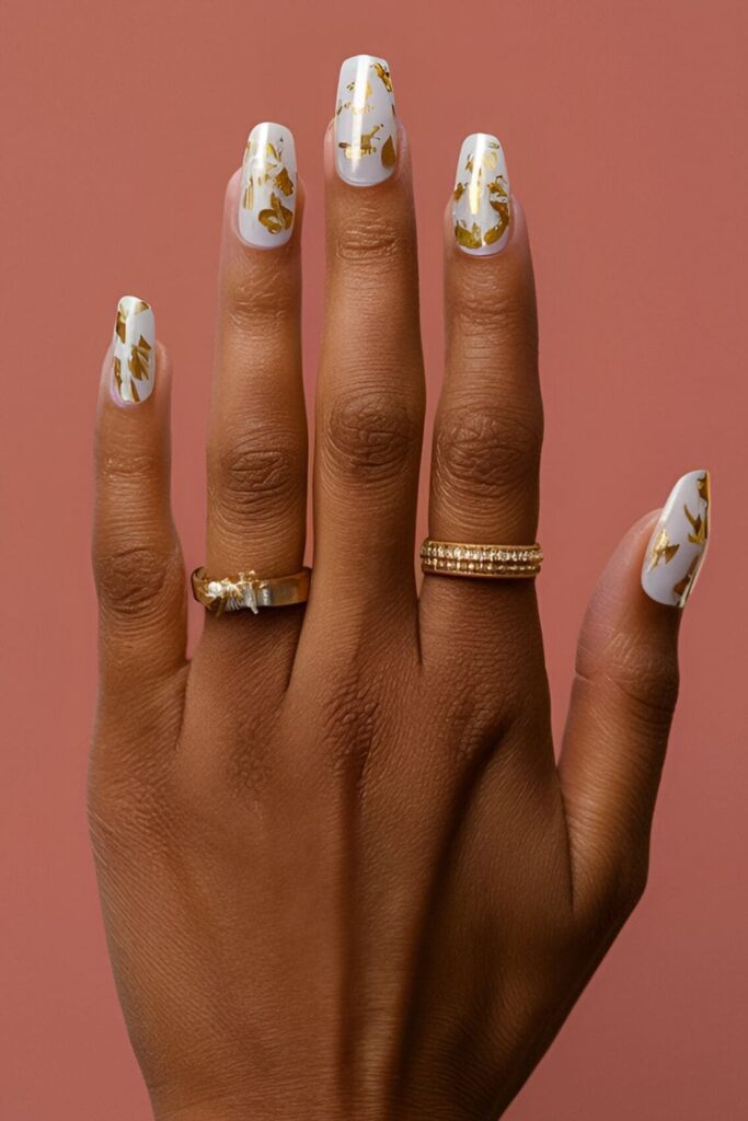 Image of hands with acrylic nails featuring a neutral base with gold flakes, adding a touch of luxury and sparkle without being too bold