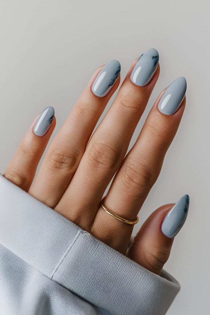 Image of hands with acrylic nails in a light blue shade with small splashes of dark blue pastel colors, offering a calming and stylish look perfect for any occasion