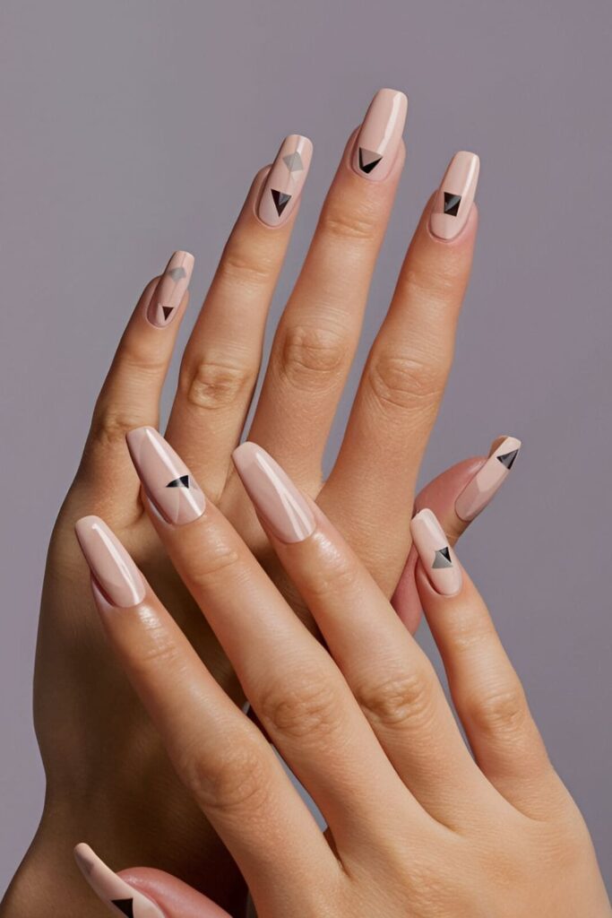 Image of hands with acrylic nails in a nude or light-colored base with small geometric shapes like triangles, squares, or diamonds in neutral tones, highlighting a modern, stylish look