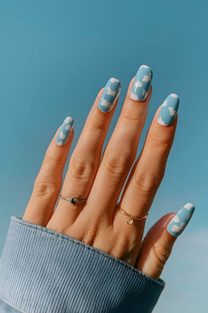 Light blue acrylic nails with white cloud patterns, creating a soft and peaceful design