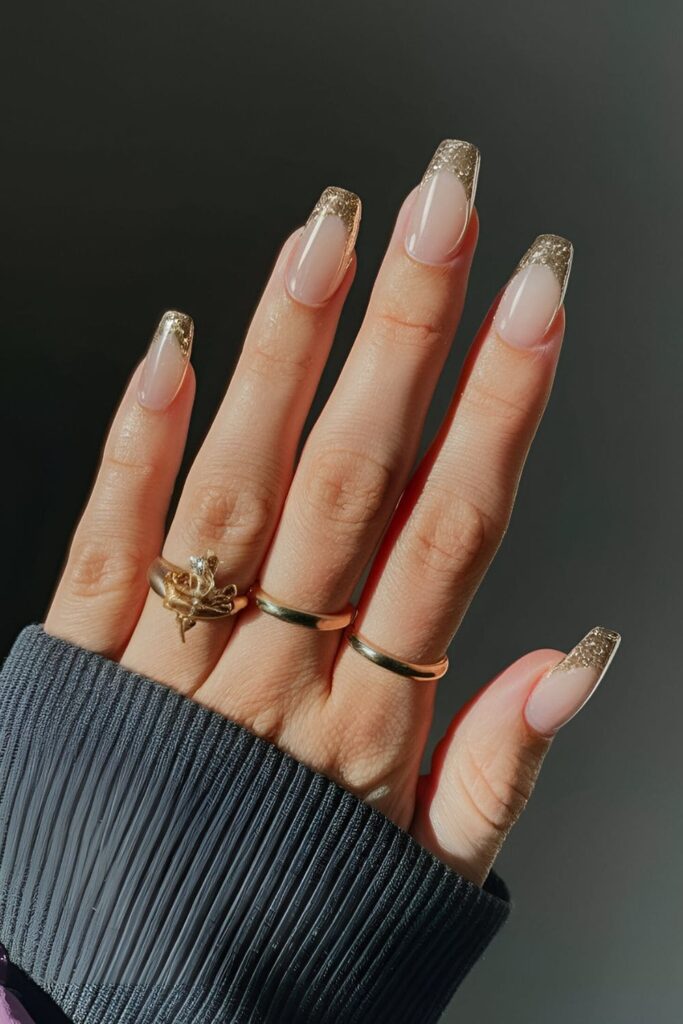 Light pink acrylic nails with gold glitter French tips, adding a glamorous twist to a classic look