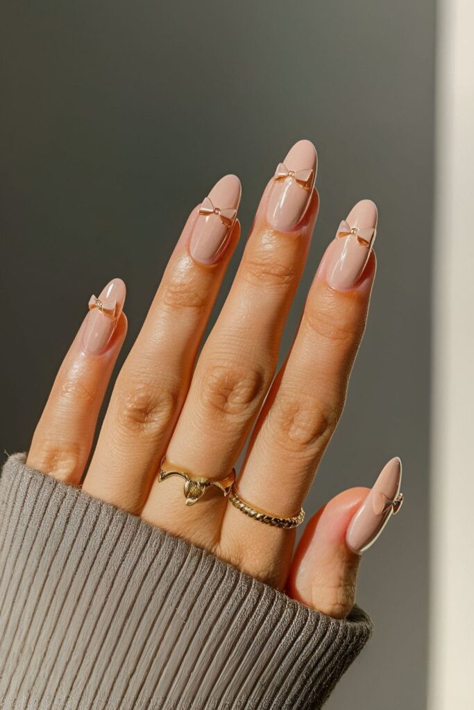 Light pink acrylic nails with tiny 3D bows on accent nails for a charming touch