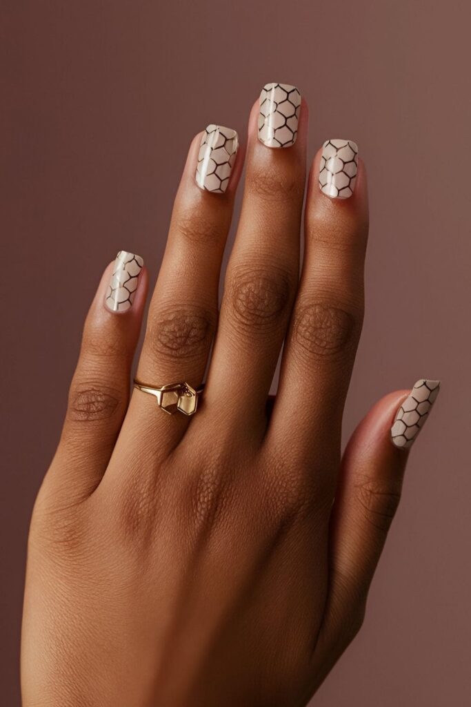 Manicure with a neutral base and small hexagon shapes in black, white, or metallic shades, creating a clean and modern look