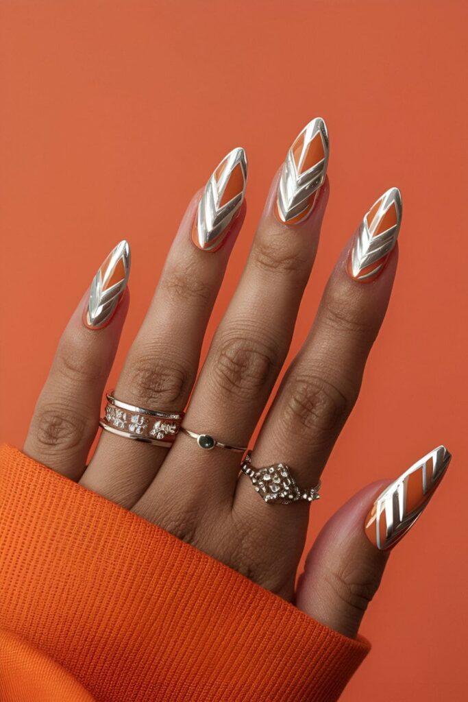 Modern silver chevron pattern on orange acrylic nails, luxurious and contemporary nail art