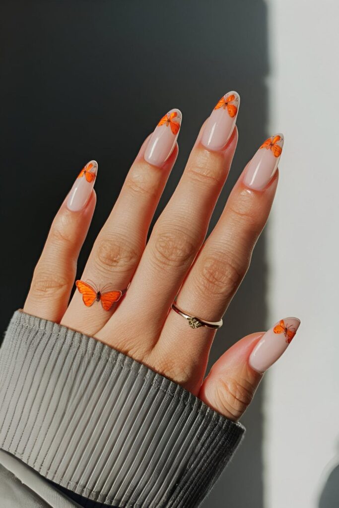 Nails adorned with delicate orange butterfly designs on a clear or neutral base, elegant and whimsical nail art