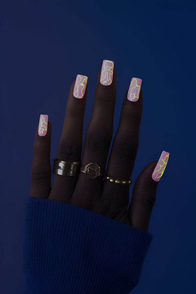 Nails painted with neon or phosphorescent polishes, featuring glowing patterns or shapes visible in the dark