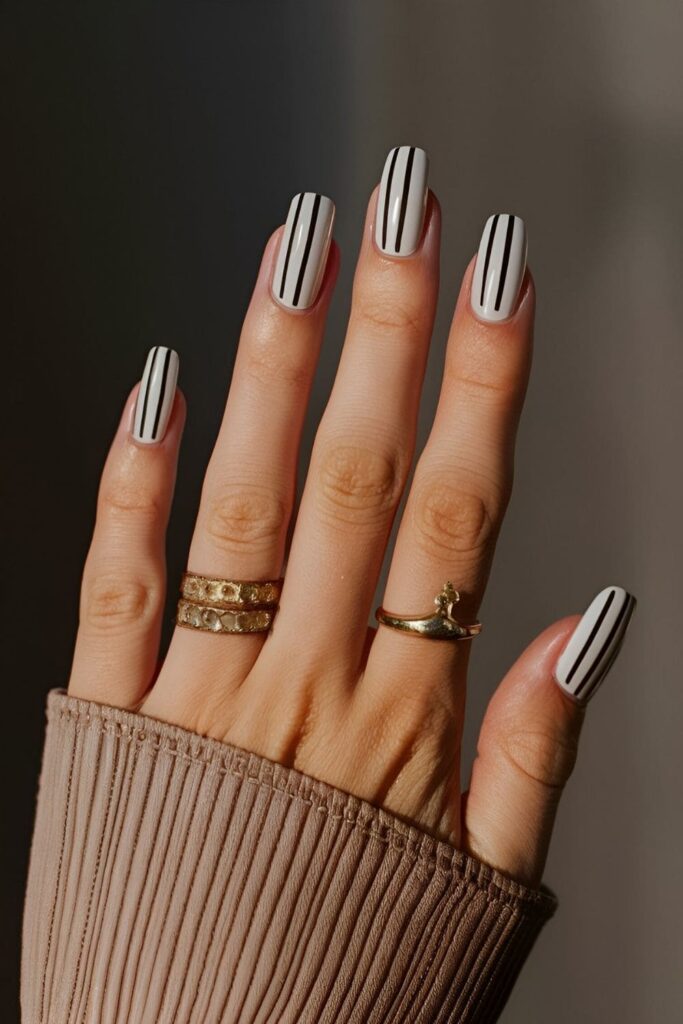 Nails with a neutral base and thin contrasting stripes (black or white) arranged horizontally, vertically, and diagonally