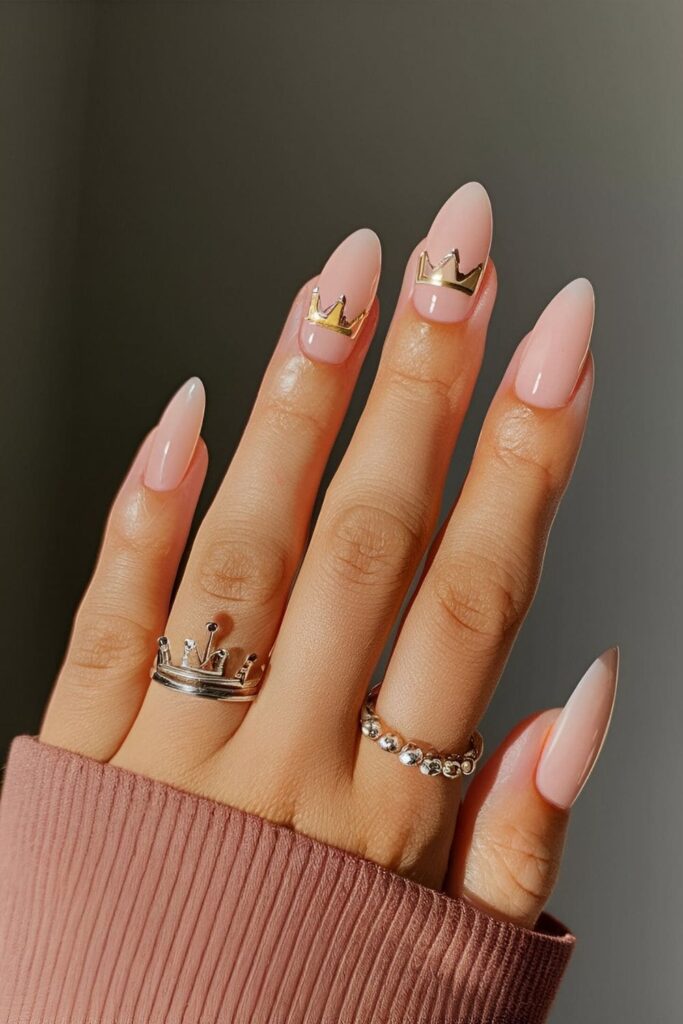 Nails with a nude base and a small crown shape in gold or silver, offering a subtle and regal minimalist touch