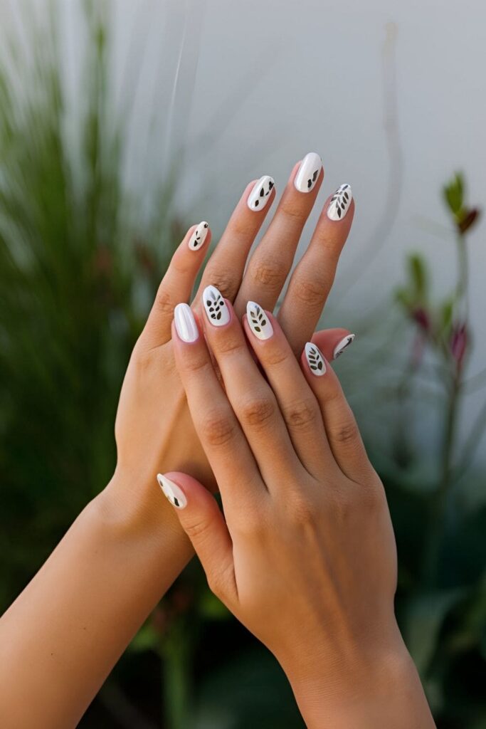 Neutral base nails featuring small leaf and vine shapes in black, white, or metallic shades for a delicate nature-inspired design