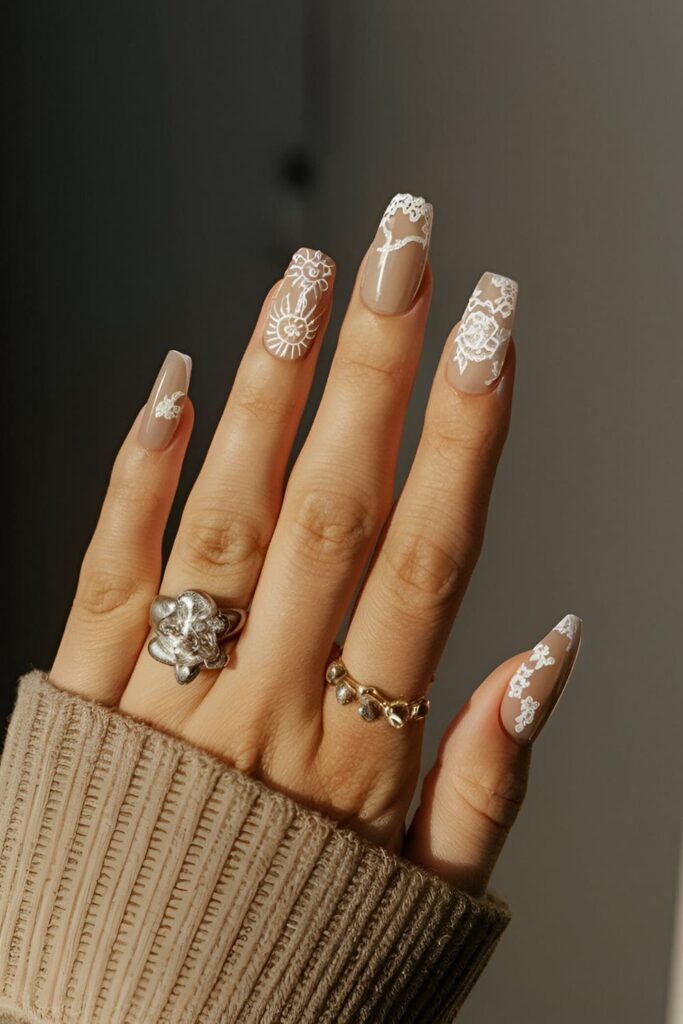 Nude acrylic nails with intricate white lace patterns, perfect for a sophisticated appearance