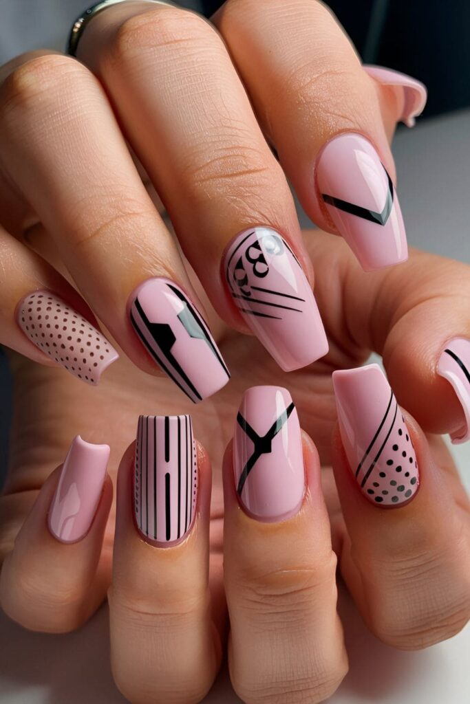 Pink coffin nails with bold black accents, including stripes, dots, and intricate designs