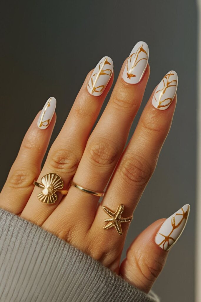 Playful gold acrylic nails with seashell patterns in white and pastel polish, perfect for summer and beach vibes