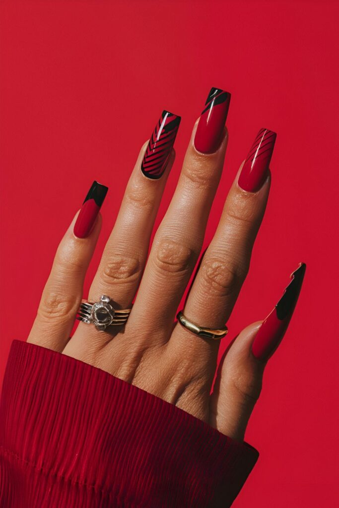 Red nails with bold black accents including stripes, dots, and abstract designs, creating a dramatic and striking look