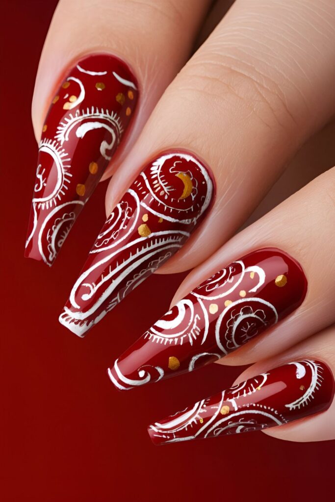 Red nails with intricate paisley designs in white or gold, looking detailed and elegant