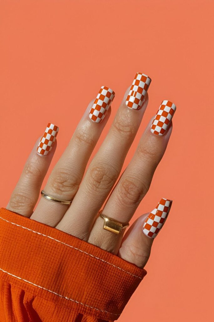 Retro white checkerboard pattern on orange acrylic nails, fun and vintage-inspired nail art