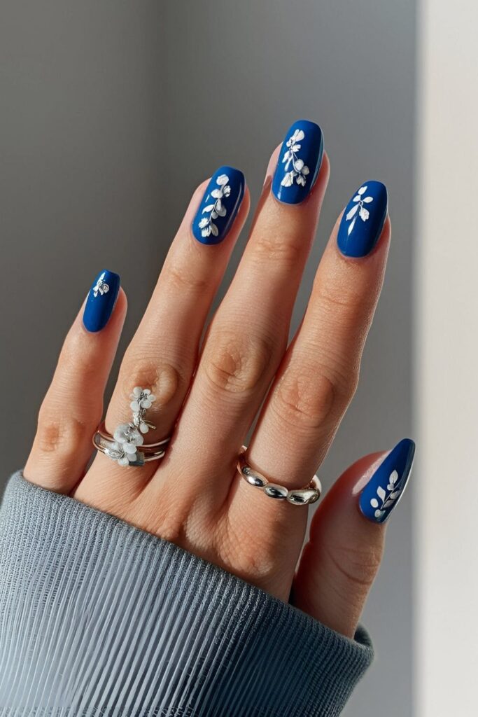 Royal blue nails decorated with delicate white or silver floral designs, adding femininity and elegance with tiny painted flowers