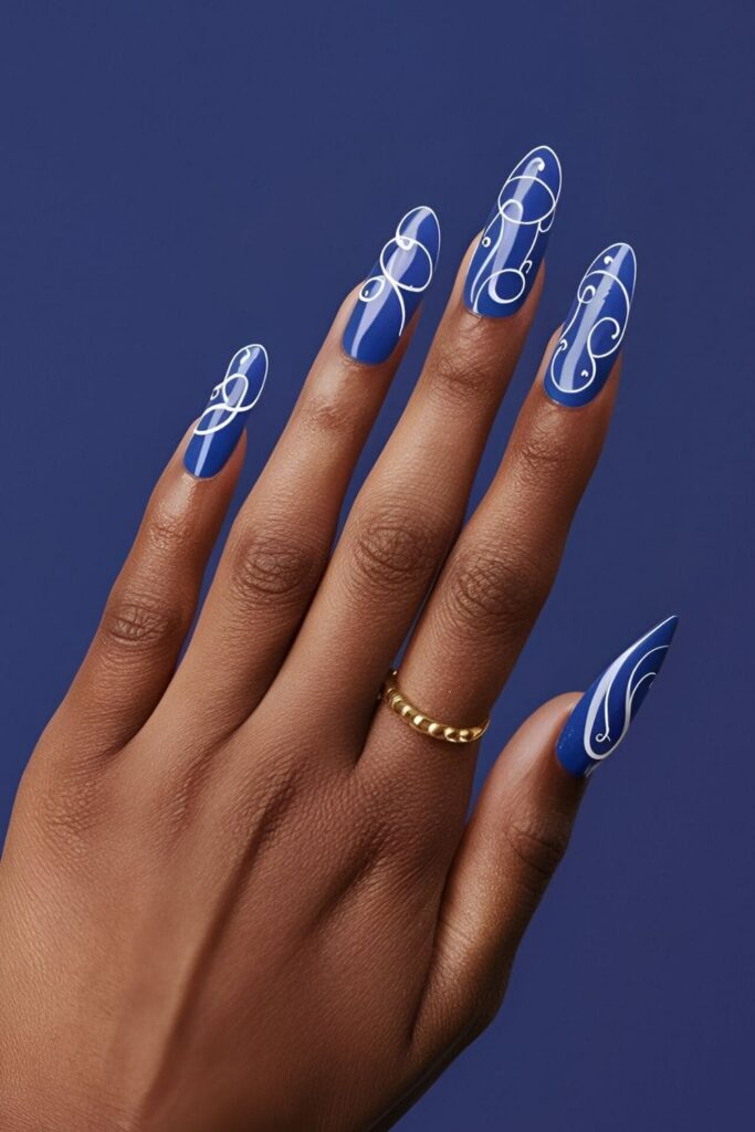 Royal blue nails with intricate white swirls and curves, creating an artistic and elegant design for a stylish appearance