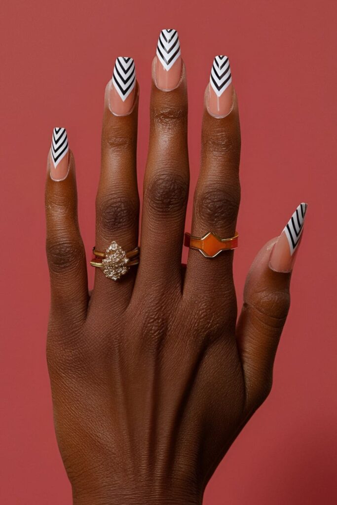 Dark-skinned hands with chevron pattern acrylic nails, featuring high-contrast zigzag designs in vibrant colors