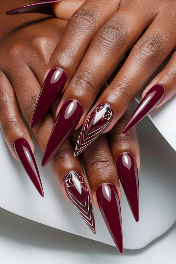 Dark-skinned hands with long, pointed stiletto acrylic nails in deep burgundy and bold designs