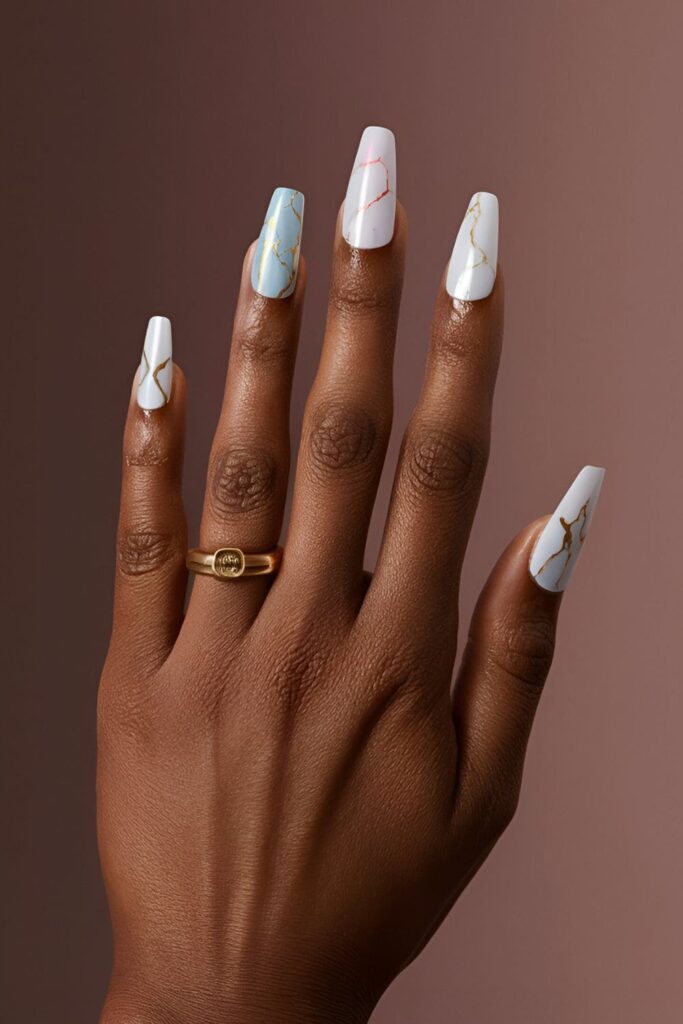 Dark-skinned hands with white marble and colorful marble effect acrylic nails, featuring gold veins