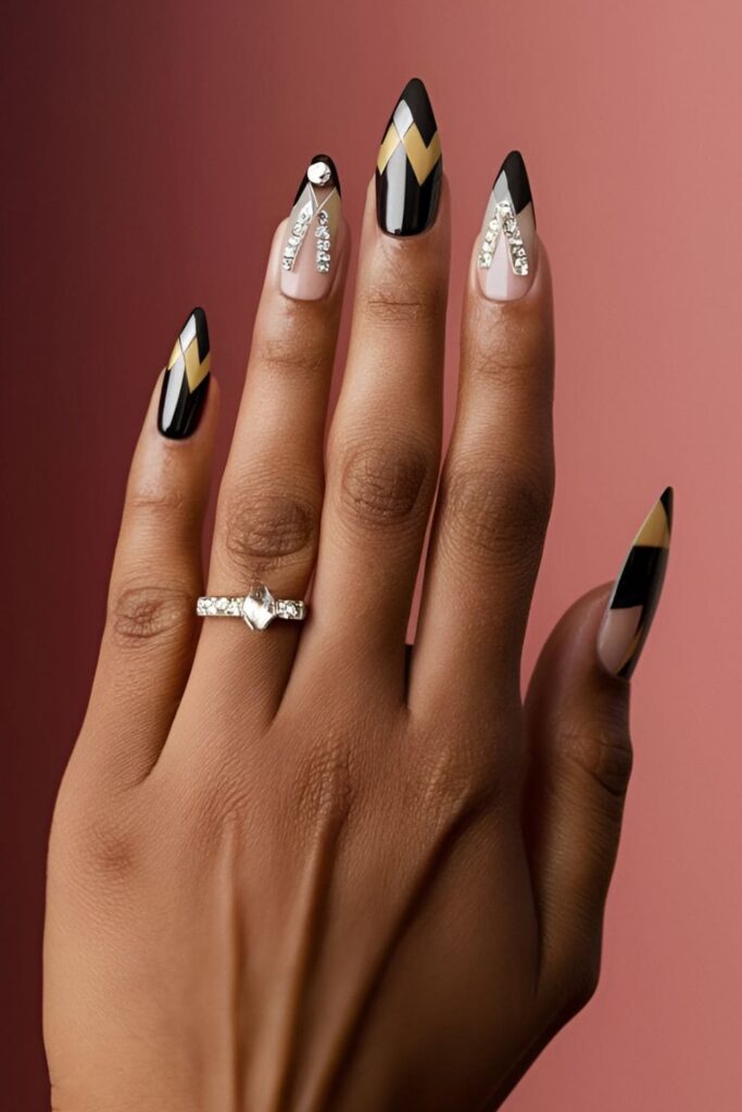 Art deco-inspired acrylic nails with geometric shapes and bold lines, using black, gold, and silver, enhanced with rhinestones for an elegant, sophisticated look