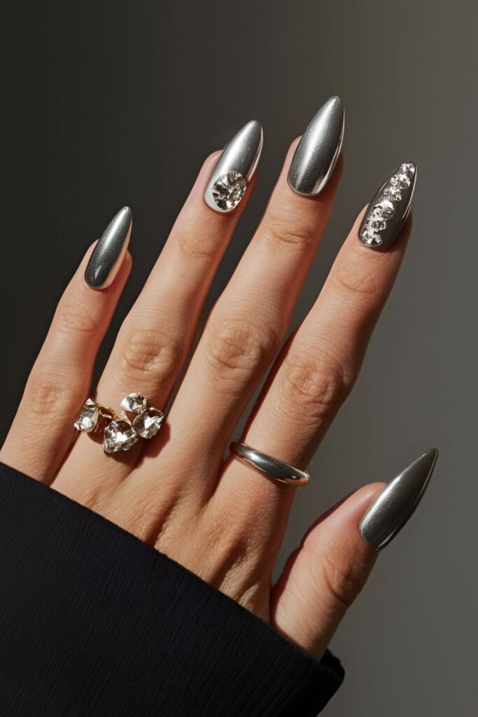 Bold, futuristic metallic acrylic nails with silver or gold polish and rhinestones, creating a striking look perfect for nights out