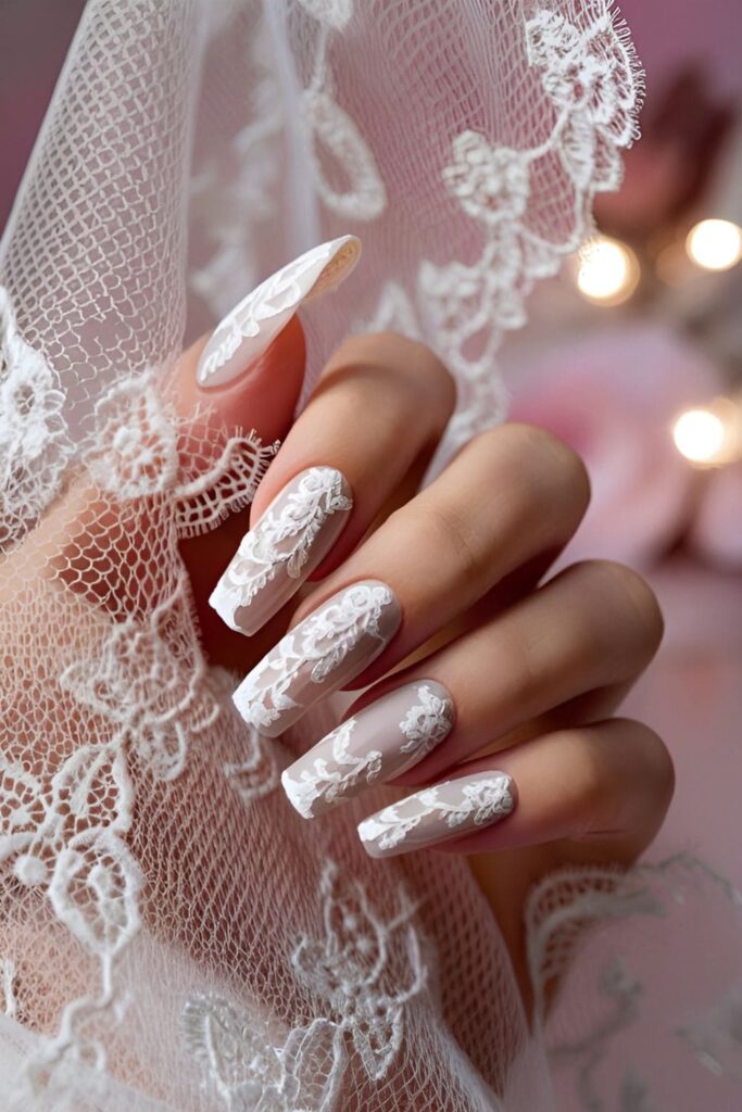 Close-up of acrylic nails with intricate white lace patterns on a nude base