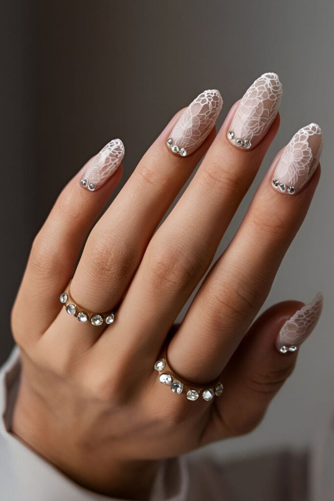 Intricate lace pattern acrylic nails with fine lines and delicate details, complemented by rhinestones for a glamorous touch, featuring white lace on a nude base