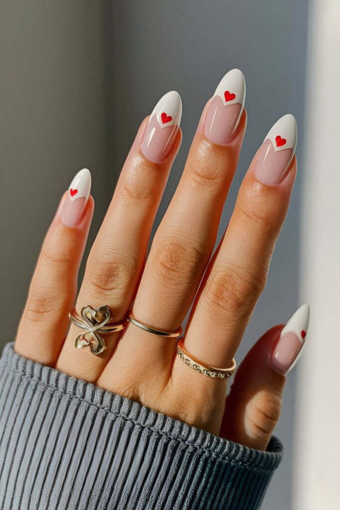 Classic French tips on nude nails featuring tiny heart designs in soft pastel colors, adding a romantic and playful detail