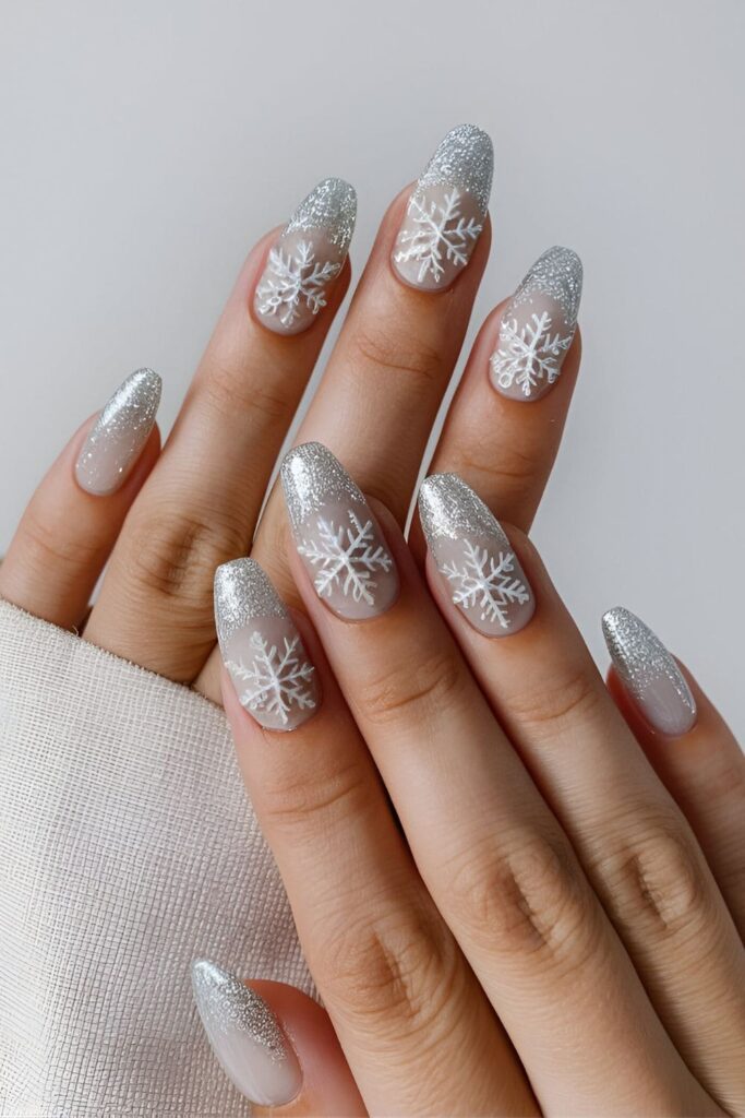 Nails featuring delicate white snowflakes over a neutral base with shimmering silver glitter accents