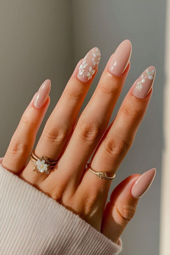 Nude nails decorated with delicate soft pink and white floral designs, accented by subtle green leaves for a romantic touch