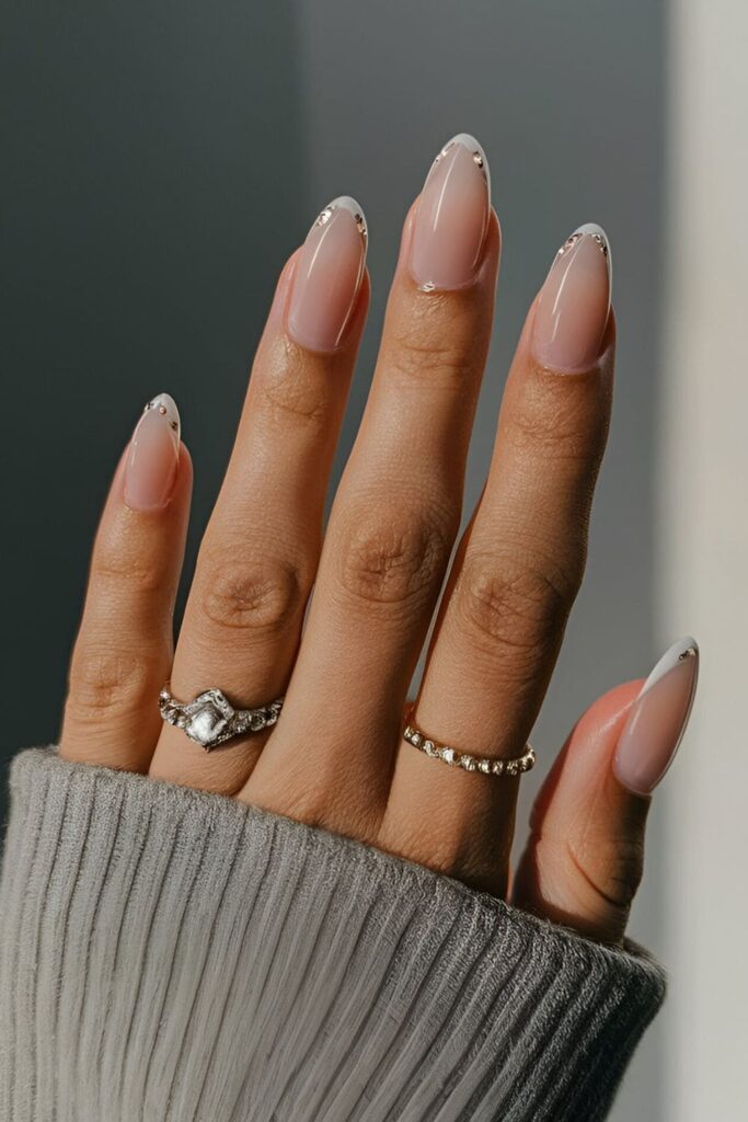 Nude nails with traditional French tips enhanced by small rhinestones at the base, adding a glamorous sparkle